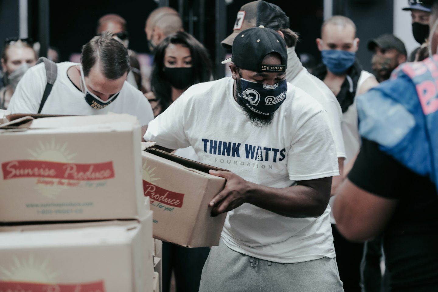 Diverse volunteers in face masks sort Sunrise Produce boxes indoors.