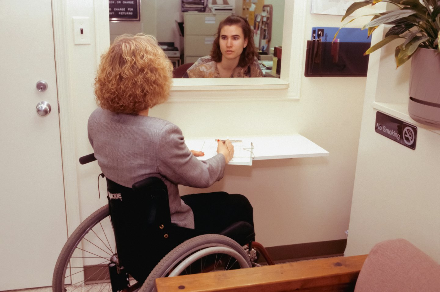 Person in wheelchair completes paperwork at service counter.